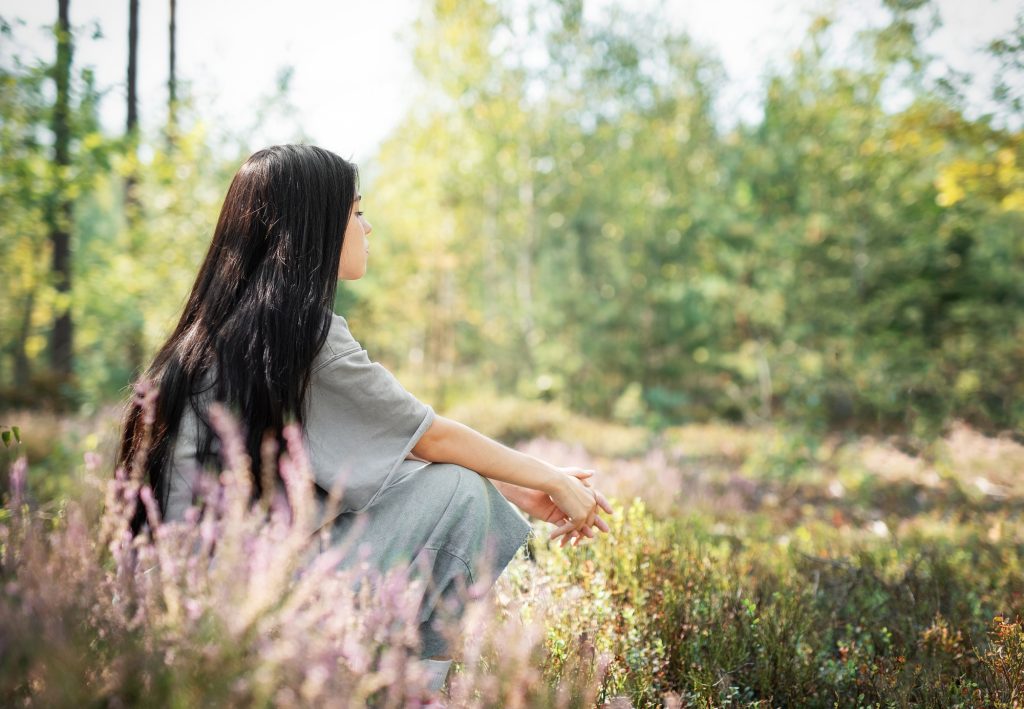 A young woman sitting peacefully in a field surrounded by wildflowers