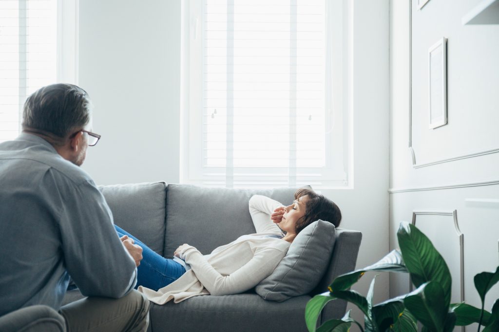 Woman at therapy room, laying on couch, discussing with psychotherapist her problems